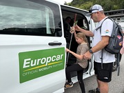 Ein Betreuer hilft einem Mädchen mit Blindenstock in einen von Europcar gebrandeten Bus