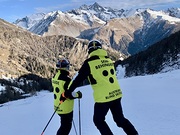 Zwei Skifahrer stehen auf einer verschneiten Piste in den Osttiroler Bergen. Ein Guide und eine sehbehinderte Person tragen gelbe Westen des Austrian Blind Ski Teams und blicken gemeinsam Richtung Großglockner .